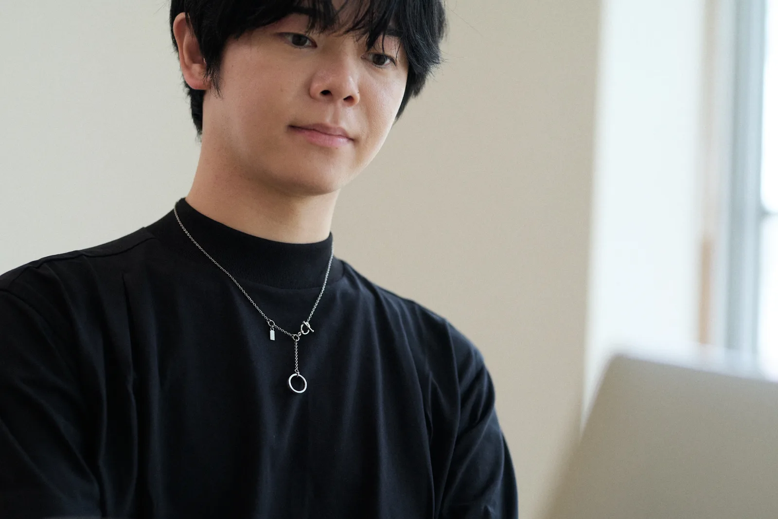 黒いTシャツにシルバーのネックレスを着けてパソコンに向かう男性